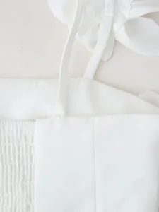 Close-up of white crop top with 3D floral decoration and fine smocked fabric texture.