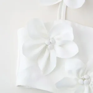 Detailed view of white sleeveless crop top with elegant handmade fabric flower decorations