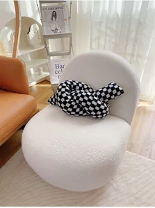 Black and white checkered knot pillow displayed on a modern white bouclé armchair
