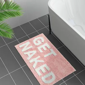 Rosa flauschige Badematte „Get Naked“ im modernen Badezimmer mit grauen Fliesen und Wanne.