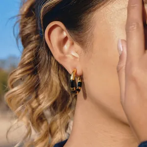 Détail d'une boucle d'oreille créole rayée noire et or en acier portée par une femme