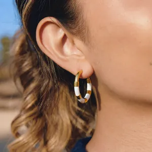 Détail de la boucle d'oreille créole en acier inoxydable à rayures dorées et blanches