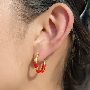 Détail d'une boucle d'oreille créole chic en acier doré et rouge sur une oreille