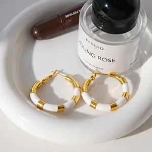 Détail des boucles d'oreilles créoles en acier doré à l'or 18 carats et blanc sur plateau