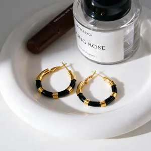 Gros plan de boucles d'oreilles créoles rayées or et noir sur une élégante assiette blanche