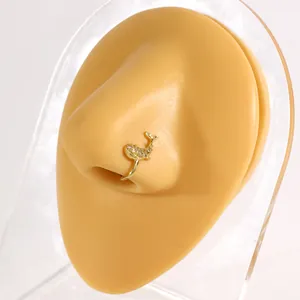 Detail view of a gold whale-shaped non-piercing nose ring with shiny zircon stones.
