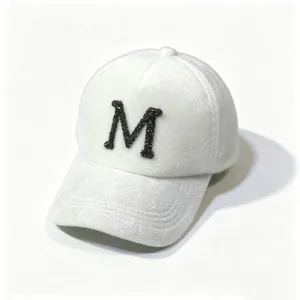 Detailed view of a white plush baseball cap featuring a black rhinestone letter M