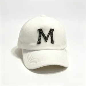 Close-up view of a soft white fuzzy baseball cap featuring a black rhinestone letter M motif