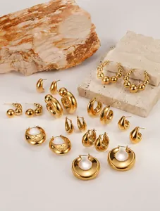 Collection of chunky gold-tone geometric earrings displayed on natural stone props