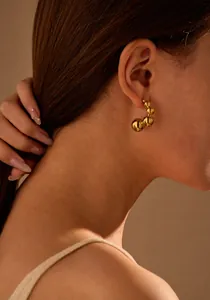 Close-up detail of a gold C-shaped beaded stainless steel earring worn on a model