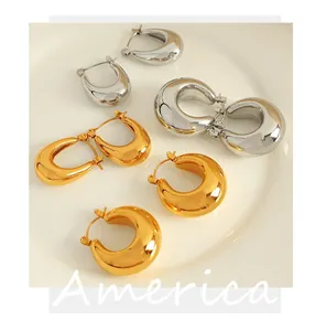 Close-up of gold and silver C-shaped titanium steel hoop earrings on a white tray