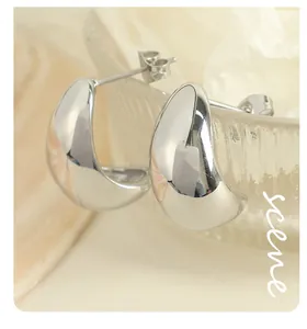 Detailed macro view of polished silver stainless steel teardrop hoop earrings on glass