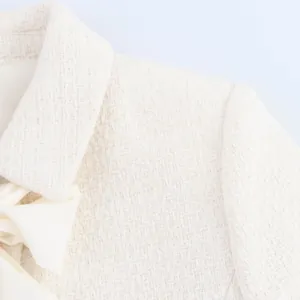 Gros plan d'un haut en tweed crème avec un détail de nœud papillon élégant à l'encolure.
