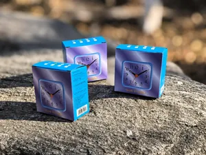 Compact square mini alarm clock shown in blue and purple cardboard packaging detail.