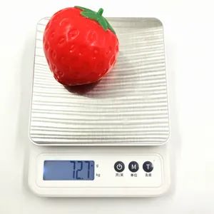 Realistic red strawberry squishy stress relief toy weighing 72.7 grams on a digital scale