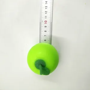 Macro view of a simulation green apple stress relief squeeze toy being measured with a metal ruler.