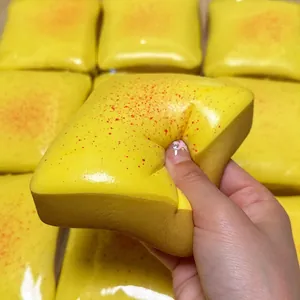 Hand squeezing a yellow mango toast squishy toy to demonstrate its soft texture