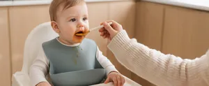 Detailed view of baby wearing a silicone bib while being fed with a spoon.