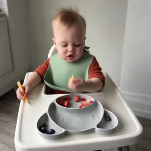 Toddler wearing a green waterproof silicone bib during a mealtime with grey plate