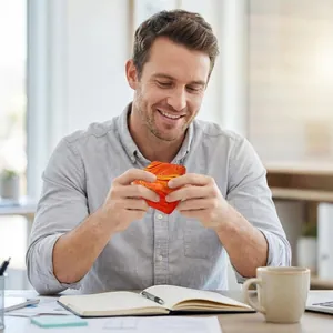 Square marbled stress relief toy in orange and yellow, being squeezed in an office setting
