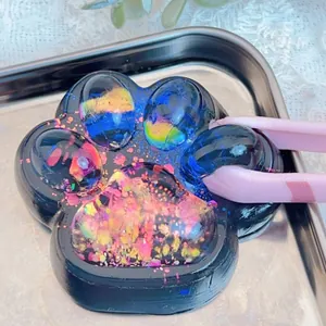 Detail view of a galaxy-style dark cat paw squishy toy being held by pink tweezers.