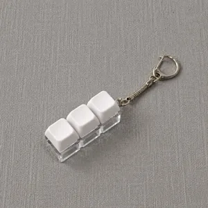 Detail of mechanical keyboard keycap keychain with three white keys and clear base.