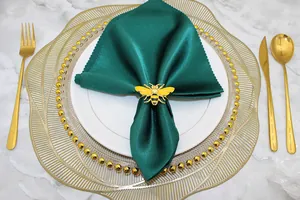 Detail view of a yellow bee napkin ring on a dark green satin napkin with gold cutlery
