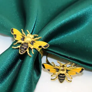 Close-up of elegant yellow enamel bee napkin rings on green satin cloth table decor