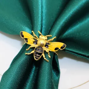 Macro detail of a golden bee napkin ring with yellow and black enamel finish on green fabric.