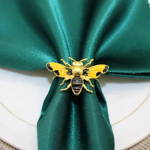 Close-up detail of golden bee napkin ring with yellow enamel on dark green satin