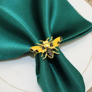 Close-up of a yellow enamel bee napkin ring cinching a luxurious green satin napkin