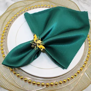 Detailed macro view of a golden bee napkin ring holding a dark green satin napkin