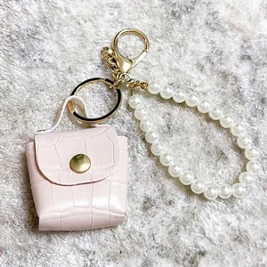 Detalle del mini llavero de bolso rosa con elegante correa de perlas blancas.