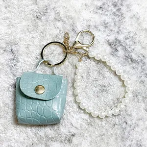 Vista detallada del mini bolso llavero turquesa con grabado de cocodrilo y tira de perlas