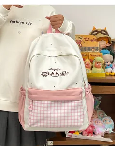 Close-up of cute cat embroidery and pink plaid pocket on a white student school backpack.
