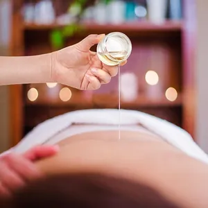 Clear 10ml glass cosmetic jar pouring massage oil on back in professional spa setting.
