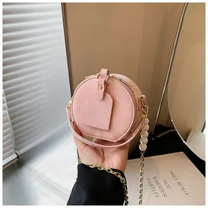 Primer plano de un mini bolso bandolera rosa redondo para niñas con elegante cadena de perlas