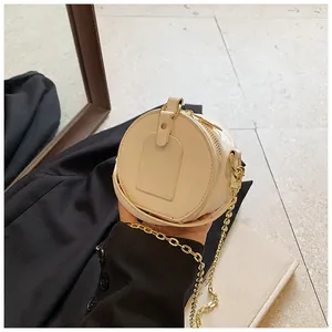 Vista detallada de un mini bolso bandolera redondo crema con cadena dorada sostenido en la mano