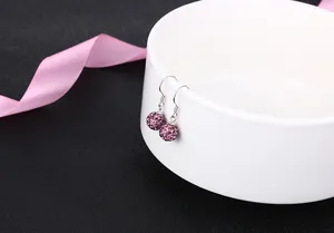 Elegant detail shot of purple crystal shamballa bead drop earrings on a white bowl.