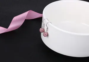 Close-up of pink crystal ball Shamballa earrings delicately hung on a white ceramic bowl