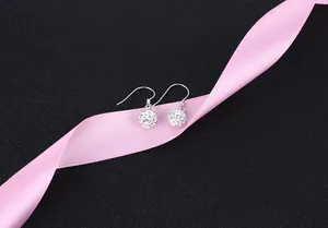 Close-up of silver crystal ball drop earrings on a pink silk ribbon and black background.