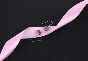 Detailed macro view of S925 sterling silver crystal pave ball earrings on pink ribbon