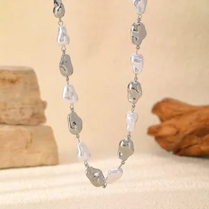 Close-up detail of a baroque pearl necklace featuring irregular silver metal beads on sand