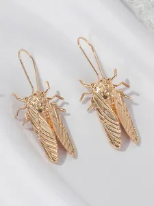 Detailed macro view of gold-finished cicada drop earrings on elegant white silk fabric