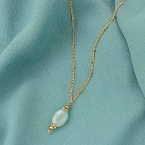 Close-up of a minimalist gold chain necklace featuring a faceted green stone pendant