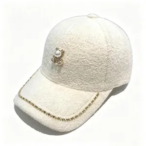 Close-up of white plush baseball cap with pearl bear and rhinestone chain detail