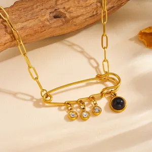 Close-up of gold safety pin pendant necklace with dangling crystal and black stone.