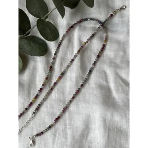Close-up of multi-color faceted natural stone beads and metal clasp on a white linen background.