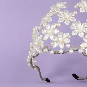 Elegant handmade bridal headband with white pearls and plastic flower petals on purple background.