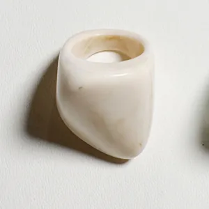 Primer plano de un anillo de acrílico blanco crema con diseño geométrico elegante